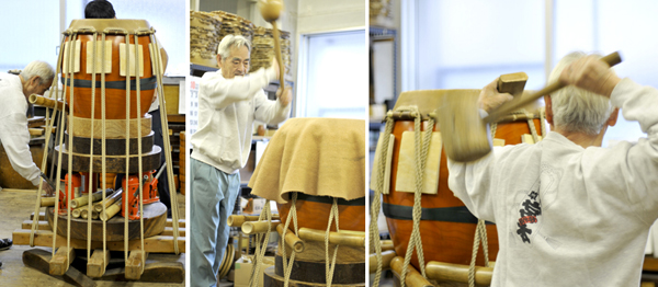 写真：親方　坂本ｘｘさんとｘｘｘさんの2人がかりで太鼓に革を乗せて、”これでもか！”というくらいに伸ばしていきます。 台の下にはジャッキ、かけられたロープにはねじっていくための竹。 上から、側面から革をたたいては伸ばしていきます。