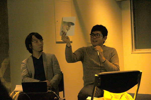 松村さんがおだやかーにトーク中。手にしているのは後述するご本人がが作った牛乳屋”いそさん”の本。 台東スタディーズ２・ファイナルにて主催者の今村さんの横で。 写真：Yui (Lwp-Magazine　ライター) 